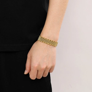Close-up of a wide golden link chain bracelet in watch band style worn on a wrist