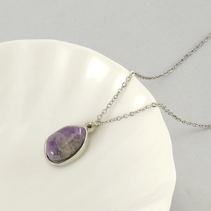Close-up of irregular natural purple stone pendant on a silver necklace in a shell tray