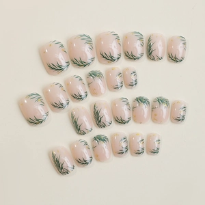 Short square press-on nails in nude pink with green leaf designs and gold foil accents