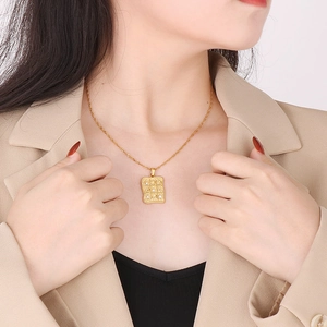Gold rectangular pendant necklace with irregular moon and sun patterns on a model