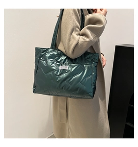 Detail of dark green quilted tote bag with padded texture and fashion label shown on model