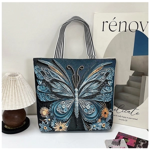 Close-up of blue butterfly embroidery on a dark denim tote bag with striped handles