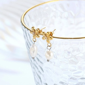 Elegant gold flower pearl drop earrings with crystal accents on a glass vessel edge