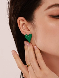 Close-up of vibrant green heart stud earrings and gold ring with black gemstone on model