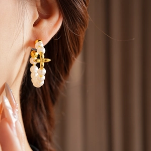 Detail of 18K gold-plated hoop earrings with pearls and golden cross on a model