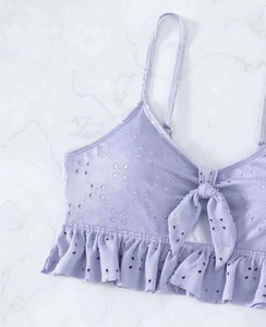 Detail van lichtpaarse bikini top met oogje borduurwerk, strik en ruches op marmer
