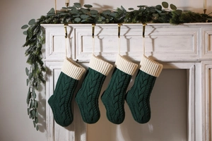 Close-up of four dark green knitted Christmas stockings hanging on a white fireplace mantle
