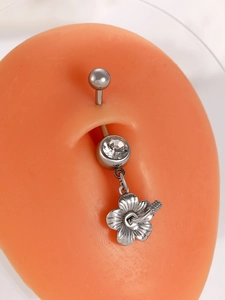 Macro shot of stainless steel navel ring with crystal stud and floral dangle charm