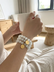 Detail of multi-layered cat eye stone bracelet with gold Fu charm on wrist