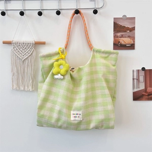 Detail of plaid tote bag featuring a yellow flower charm and geometric woven strap