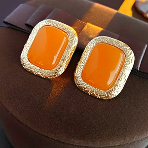 Vintage style gold and orange rectangular stud earrings with textured borders on jewelry box