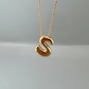 Macro detail of a 3D letter S pendant with golden finish on a fine O-link chain