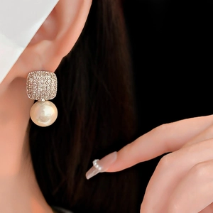 Detail of square zircon and round pearl earrings worn by a model on dark backdrop