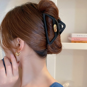 Pince à cheveux triangulaire noire mate et boucles d'oreilles dorées portées sur modèle