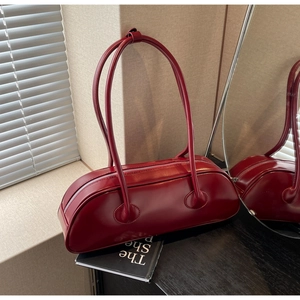 Detailed view of burgundy cylindrical shoulder bag with silver zipper and slim double straps