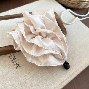 Détail de la pince à cheveux fleur en satin beige avec plis et base noire en goutte