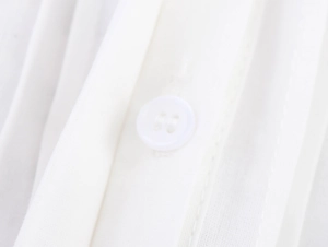 Dettaglio ravvicinato del bottone bianco e del ricamo raffinato sulla camicia bianca
