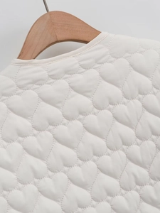 Detail of white satin jacket featuring unique heart-shaped quilting and a round neckline