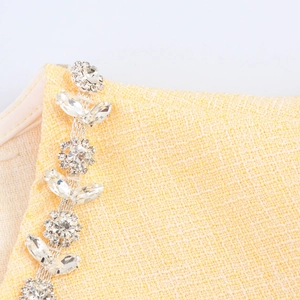 Dettaglio vestito in tweed giallo con catena di cristalli e trama floreale