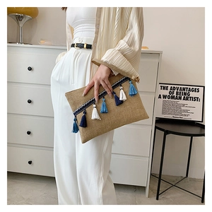 Detail view of woven straw envelope clutch with blue tassels and natural flax texture