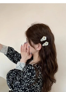 Detail view of two white flower hair clips worn on side of wavy dark brown hair