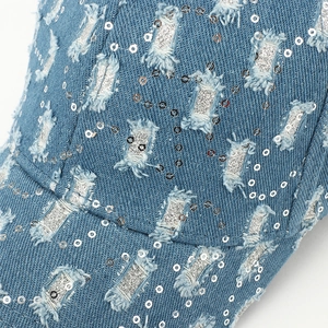 Détail macro d'une casquette en jean déchiré avec paillettes argentées et texture brillante