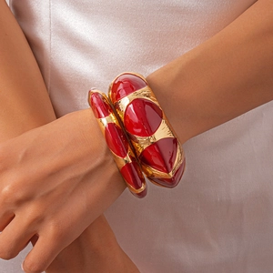 Detail of vintage red enamel and gold metal geometric bangles worn on a model's wrist