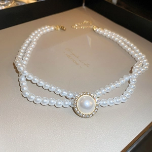 Détail d'un collier de perles double rang avec un pendentif central serti de diamants