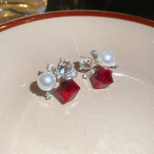 Macro detail of silver floral stud earrings with red crystal, pearl, and zircon stones