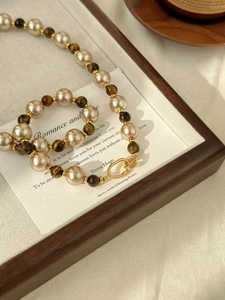 Close-up of vintage pearl and tiger eye stone necklace with golden textured toggle clasp