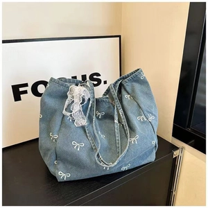 Detail of blue denim tote bag with white bow pattern and delicate lace bow charm