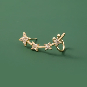 Close-up of golden metal ear cuff with four zircon stars on a dark green background
