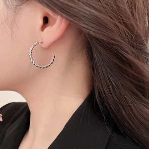 Close-up of a silver twisted rope hoop earring worn on a female model for a chic look