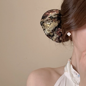 Detailed close-up of a vintage black brocade hair tie with gold and pink floral embroidery