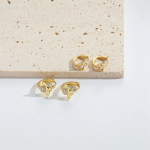 Detail of gold floral and bee earrings with transparent stones on a travertine stone