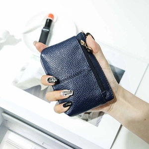 Mini portamonete in pelle litchi blu navy con cerniera dorata su sfondo di rivista