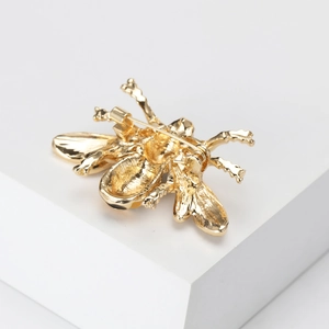 Elegant gold metal bee brooch with yellow enamel detail on a clean white display stand