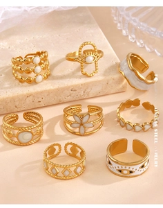 Close-up of gold stainless steel rings with white enamel flowers and evil eye details