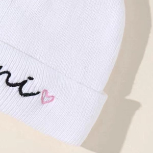 White ribbed knit beanie for kids with black mini text and pink heart embroidery