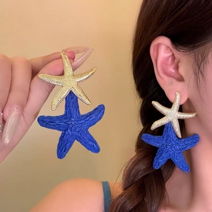 Detailed view of oversized blue woven and gold starfish earrings in bohemian style.
