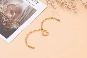 Close-up of golden hollow heart charm bracelet with bold ring chain on warm background