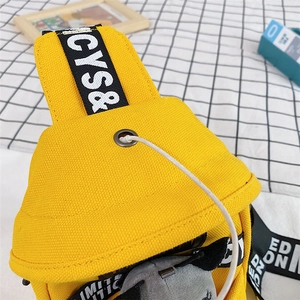 Detail of yellow canvas chest bag showing the metal earphone hole and lettered strap