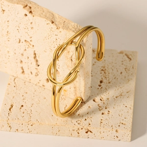 Detail of a gold knot cuff bracelet with a polished finish on a travertine stone background