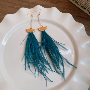 Dettaglio di eleganti orecchini a piuma blu lago con ganci dorati su un piatto bianco