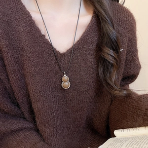 Close-up of a long leather cord necklace with a vintage gourd pendant on a brown sweater