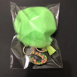 Detail of green faux fur pompom keychain with letter S resin charm and matching tassel