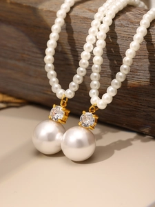 Detail of white pearl earrings with gold metal and cubic zirconia on dark wood