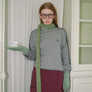 Red-haired model wearing a green chunky knit scarf and grey sweatshirt in a stylish studio