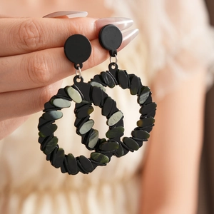 Detail of geometric drop earrings featuring black round frames and dark green oval stones