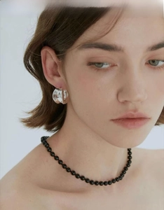 Close-up of irregular silver hoop earring and black beaded necklace on a model